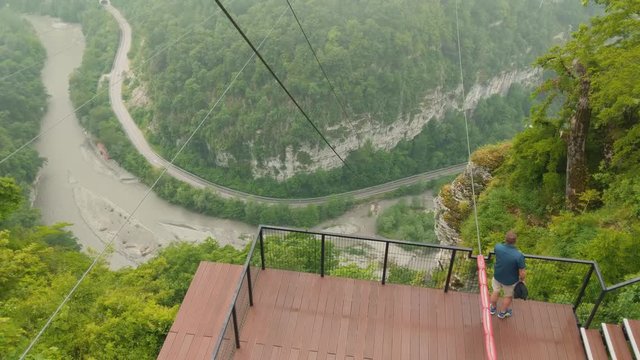 a man stands on an observation deck in a gorge in the mountains and looks down at the river and the road