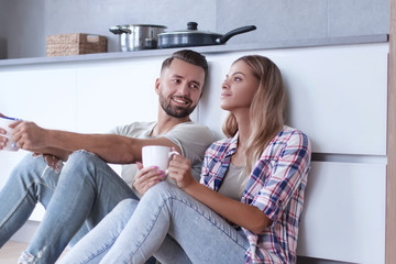 young couple drinking coffee sitting on the kitchen floor