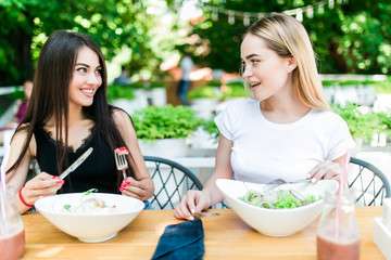 Two girls have lunch in a cafe. Two girls eat salad in cafe.