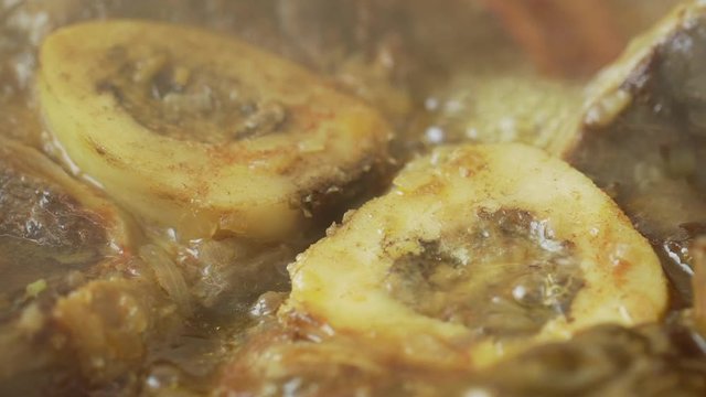 Slow motion closeup of delicious osso buco marrowbone cooked in a hot pan in a restaurant or in the kitchen of a house.