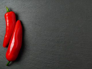Two red chilly peppers on a left side of a black slate plate, Copy space.