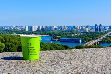 Paper glass of coffee on stone parapet in front of Kiev cityscape. View on residential districts on left bank of the river Dnieper in Kiev, Ukraine