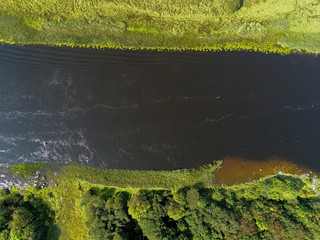 Aerial top view on a river with a field on one side and a forest on the second.