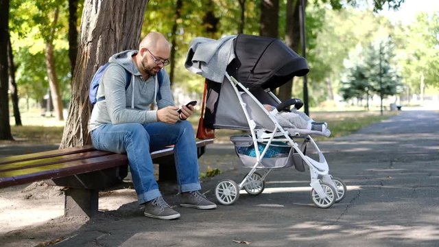 man walks with a stroller in the park. Caring father for a walk with a child with a phone in his hands
