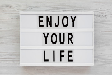 'Enjoy your life' words on a modern board over white wooden background, overhead view. Top view, from above. Flat lay.