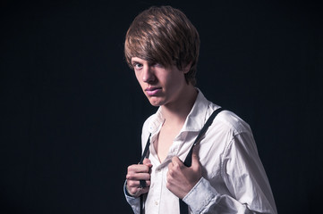 Fototapeta na wymiar Blond boy with white shirt and suspenders photographed in studio with black background