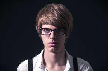 Blond boy with white shirt, suspenders and glasses photographed in studio with black background