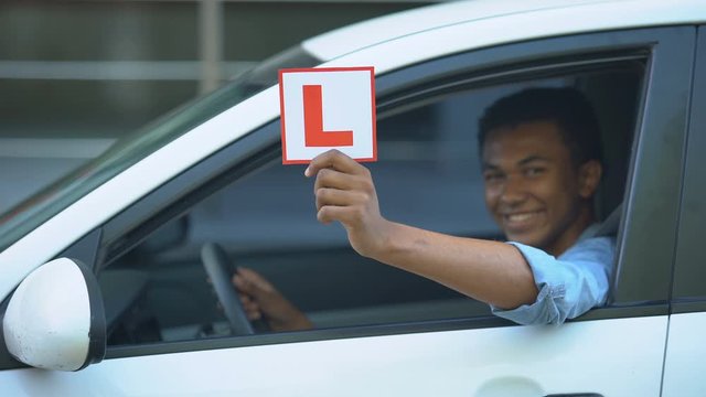Smiling boy showing l-plate at car window, driving courses, right-hand traffic