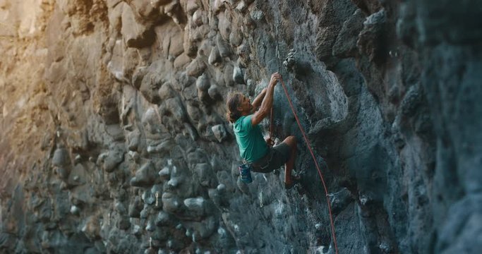 Strong male rock climber lead climbing on a sport route, clipping into a quick draw, cinematic slow motion rock climbing moments