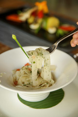 White turnip tagliatelle in a white bowl served on a wooden restaurant table. Exquisite dish. Creative restaurant meal. Fine dining concept.