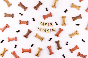 Dog food pattern made with dry snacks in shape of bones. Word dog in wooden tiles. Funny flat lay texture. Home pets, animals feeding. Special diet, training supply. Top view background.