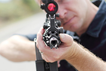 Closeup of a man aiming an assault rifle with scope.