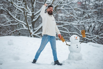 Fototapeta na wymiar Holly jolly swag Christmas and noel. Happy hipster winter portrait. Snowman. Winter portrait of young handsome hipster in snow Garden make snowman.