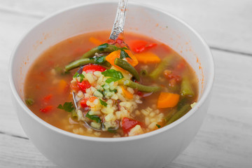 Vegetable soup in a ceramic bowl is mixed with a spoon