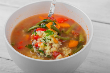 Vegetable soup in a ceramic bowl is mixed with a spoon