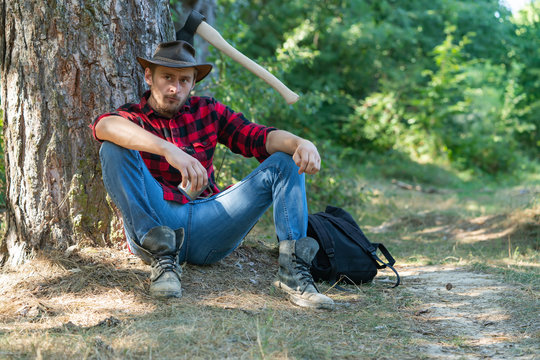 Handsome man lumberjack with a large ax examines the tree before felling. Deforestation is a major cause of land degradation and destabilization of natural ecosystems.