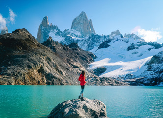 Tourist woman on Mount Fitzroy, Patagonia trek. Scenic view of snowcapped mountain tops. Blue sky, turquoise blue lake and scenic rock landscape. Shot in Argentina. Nature, travel, adventure, hiking.