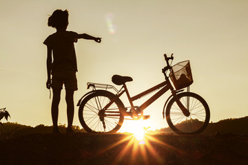 Silhouette of little girl riding bike at sunset background