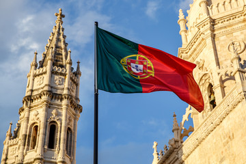 Portuguese flag waving in front of a blue sky and monastery. © 9parusnikov