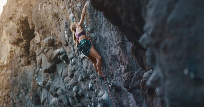 Young fit woman lead rock climbing on sport route in golden light, outdoors rock climbing, cinematic slow motion rock climbing moments