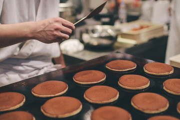 a stall vendor pouring creamy batter on a hot plate to make Dorayaki, a Japanese pancake-like dessert & a street snack popular