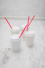 four white paper cups with red tubes for coffee to go on white wooden table in selective focus.
