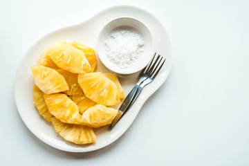 Close up of a sliced pieces of fresh pineapple served with salt with isolated white table. Adding salt to pineapple suppresses the bitter flavor of the fruit.