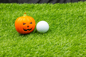 Golf halloween with golf ball and pumpkin are on green grass