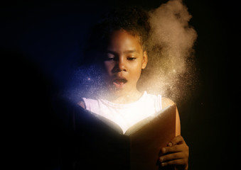 Surprised African-American girl reading magic book on dark background