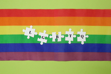 Puzzle pieces with abbreviation LGBTQ and rainbow flag on color background