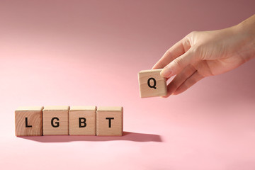 Female hand composing abbreviation LGBTQ from wooden cubes on color background