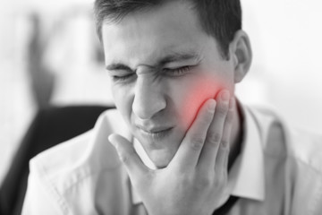 Young businessman suffering from toothache in office