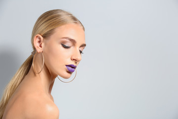 Obraz premium Beautiful young woman with bright purple lipstick on light background
