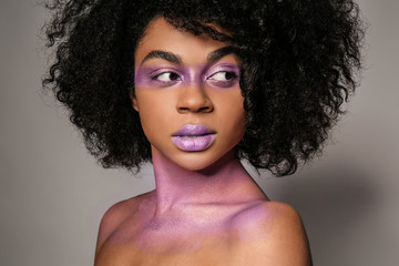 African-American woman with purple paint on her body against grey background