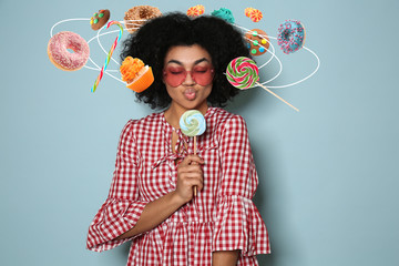 Portrait of young African-American woman with lollipop on color background