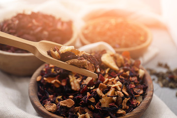 Scoop of dry tea leaves with fruits over bowl on table