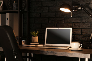 Stylish workplace with modern computer near dark brick wall at home