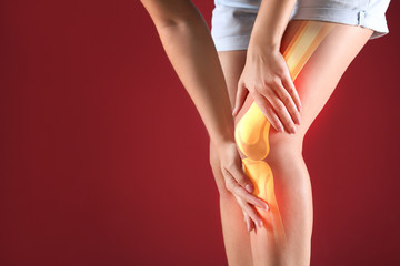 Young woman suffering from pain in knee on color background