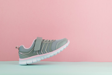 Walking grey sneaker with right foot on pink and blue background.