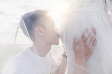 Asian husband kissing his pregnant wife’s belly with his eyes closed in mountain. Asian Married...