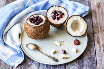 Berry dessert with yogurt in a cup of coconut on a wooden background. Blackberries, raspberries, blueberries, black currants. Blue napkin