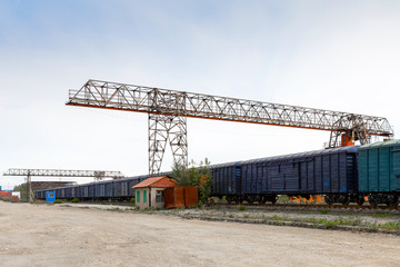 Obraz premium Large metal gantry cranes at a on the railway platform, standing on freight wagons for storing goods. Type of bearing metal structures of gantry crane against the blue sky