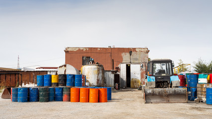 Fototapeta na wymiar Industrial zone: a large metal warehouse for storing goods, metal barrels of different colors are nearby, a tractor-loader