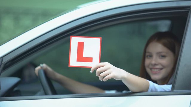 Girl sitting on driver seat in car showing l-plate, learner under instruction