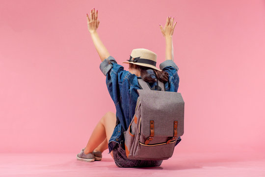 Smiling woman traveler sitting raising arms with backpack in holiday on pink backgrounds, relaxation concept, travel concept