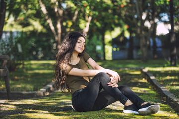 Young adult beautiful brunette girl in casual clothes happy sitting on mossy in Park