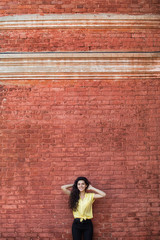 Young adult beautiful brunette girl in casual clothes on the background of a building with red brick walls