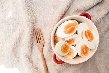 Boiled eggs cut in half, placed in a red bowl, on the tablecloth