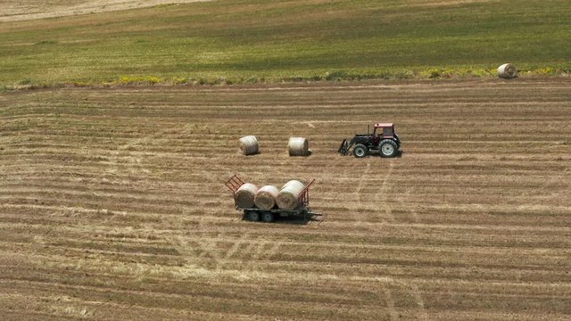 Aerial shot of a farmer driving tractor collecting and loading hay bales on a trailer