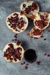 A glass of wine on a gray background among pomegranates. Close pomegranate and red pomegranate seeds. The leg of a glass goblet next to the fruit.